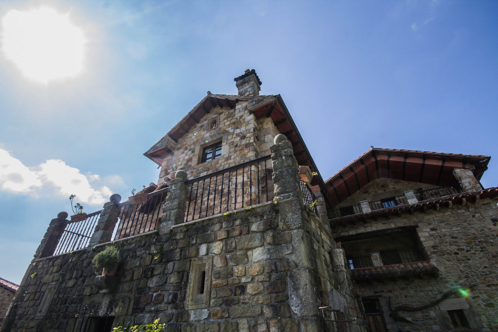 Fachada lateral de Finca Gándara en contraluz con balcón de piedra y cielo azul